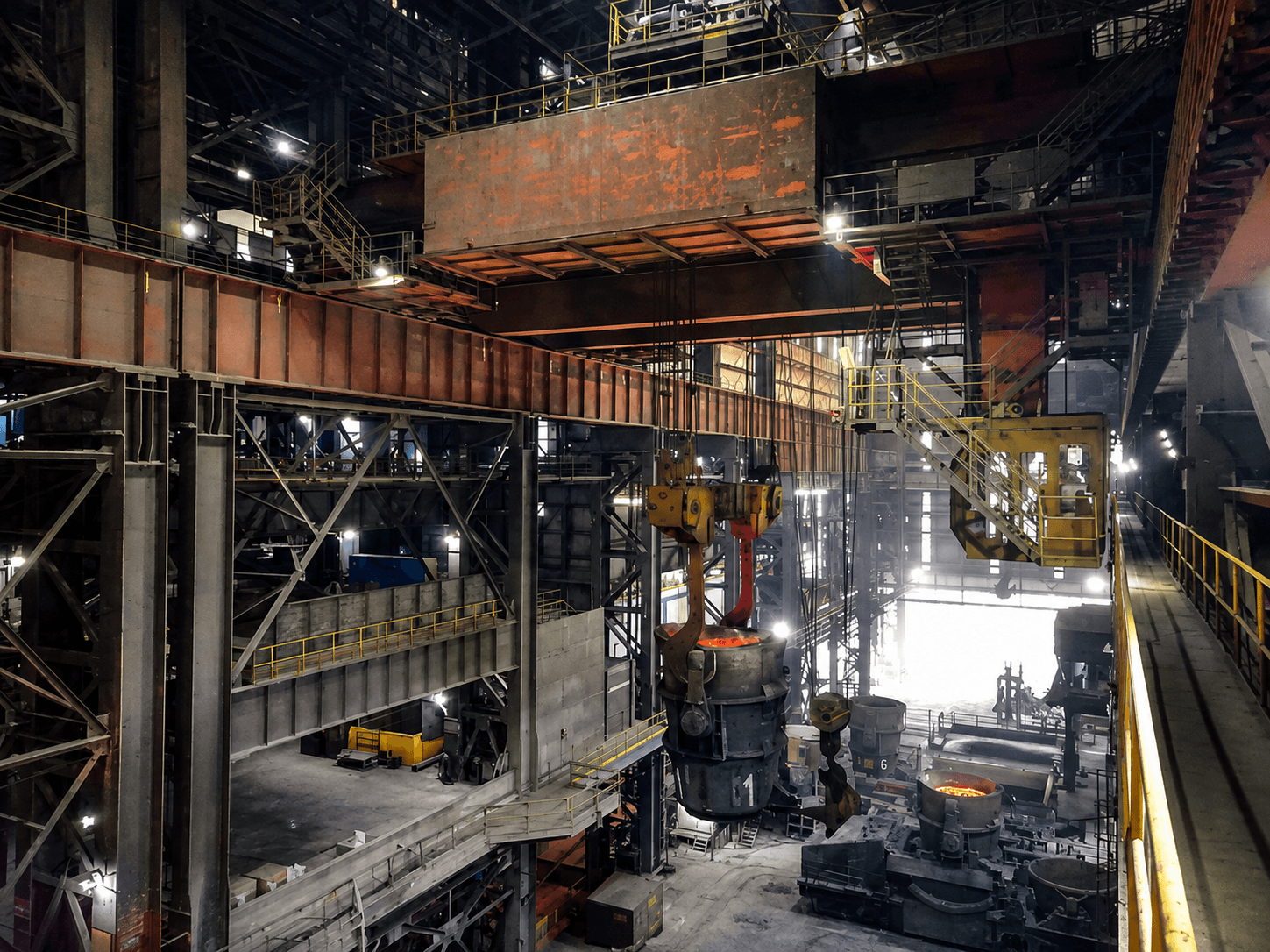 A ladle crane carrying a suspended ladle of molten steel through the bay hall.